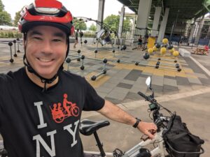 Patrick Weir wearing a red helmet on a cargo bike in New York City near a playground
