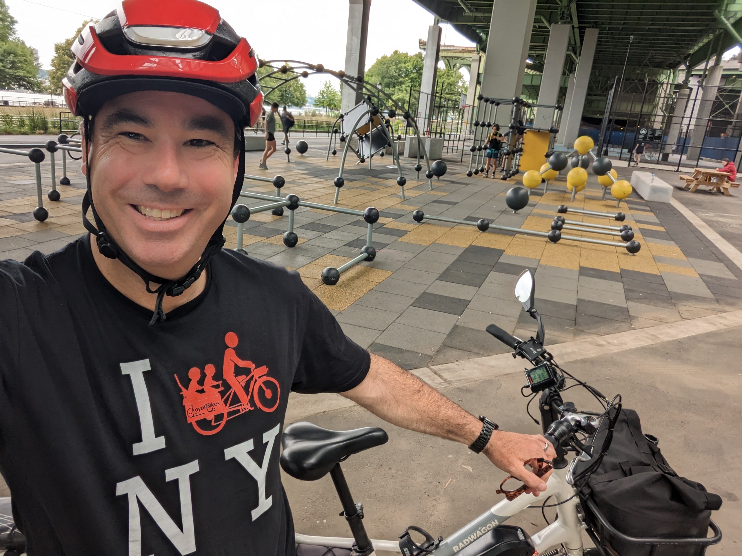 Patrick Weir wearing a red helmet on a cargo bike in New York City near a playground