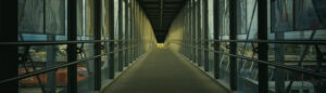 Covered pedestrian bridge over railway tracks, with light at the far end — symbolizing quiet progress and crossing into something new.